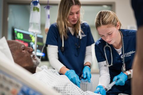Two UNH nursing students in scrubs provide care to a patient during a clinical simulation at the Health Sciences Simulation Center.