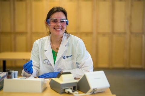 Nutrition student smiling in a lab coat and goggles