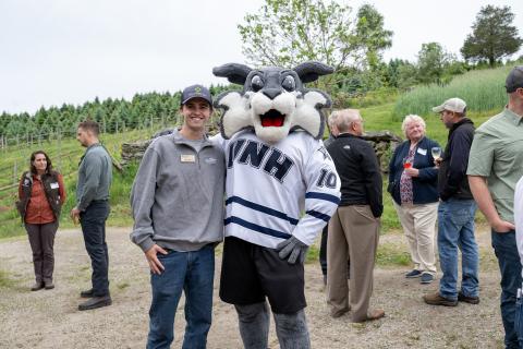 UNH student posts with Wild E Cat mascot outside with people in the background