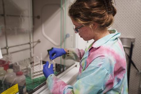 A woman in a multi-colored lab coat looks at a sample in a laboratory setting