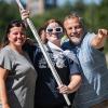 A female student in sunglasses and face paint holding a UNH flag stands between a woman and a man, with the 