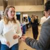 A woman with blond hair wearing a white sweater talks to a man in a suit jacket at a career fair