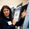A woman looks back while speaking to a guest as she explains research on a poster in front of her