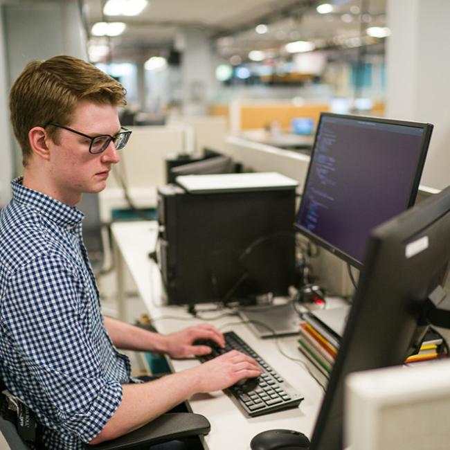 Male student sitting at computer with three monitors