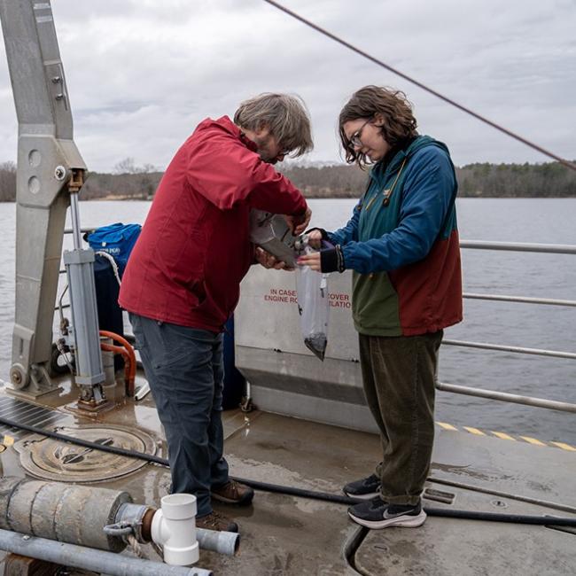 student and professor collecting samples on a boat in the ocean