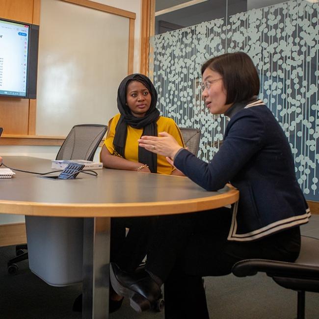 Student in yellow talking to a professor sitting at a desk