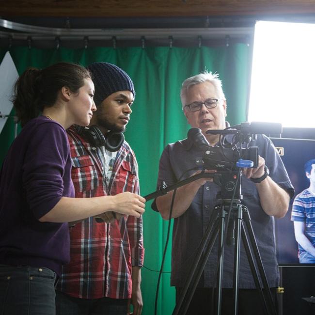 Two students and a professor looking at a camera