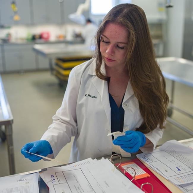 Female student in white lab coat and blue gloves collecting samples