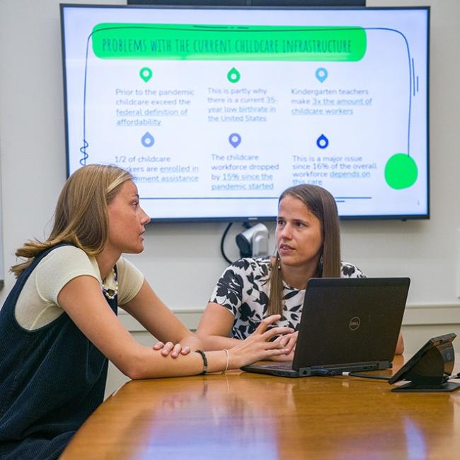 A female student and professor discussing their research together in front of a smart board