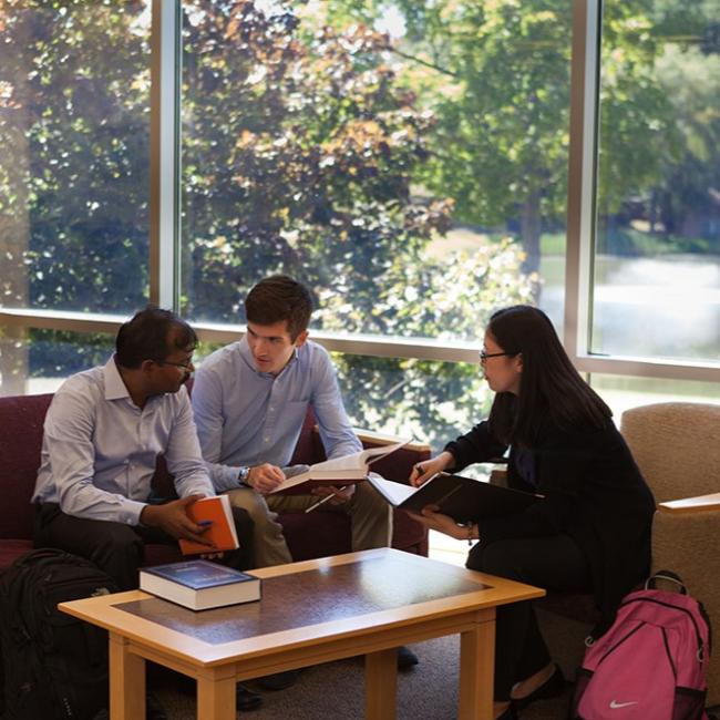 three students sitting and talking around a desk