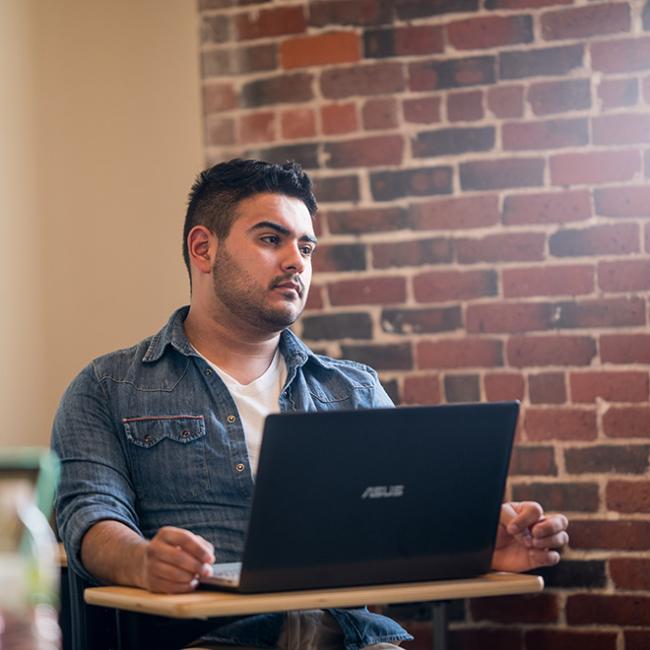 Male student sitting at a desk with a laptop in front of him