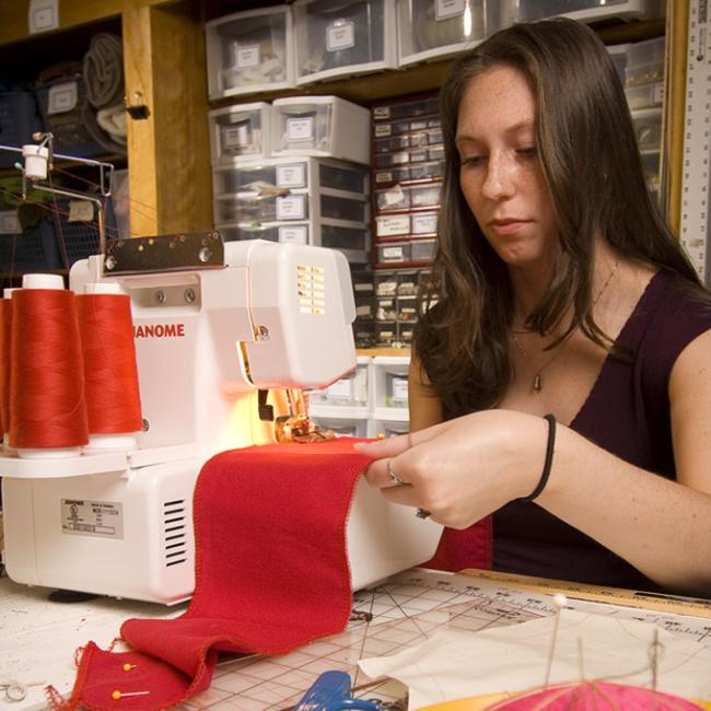 Female student running red material through a sewing machine