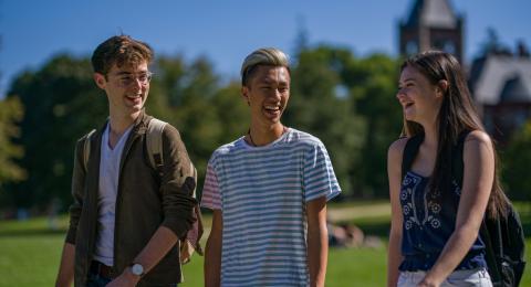 Three students walking and talking with T-Hall in the background