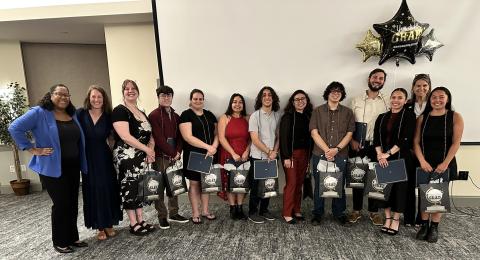 Graduating students dressed up for event, standing in front of a screen with graduation balloons, smiling with McNair staff members.