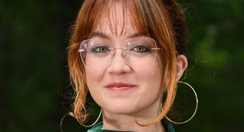 Female student with glasses and green velvet dress with trees in the background.