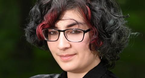 Student dressed in black with arms folded with trees in the background.