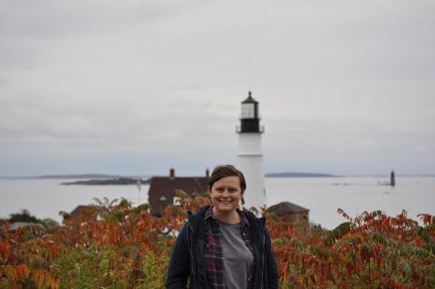 a woman with short brown hair in front of a light house