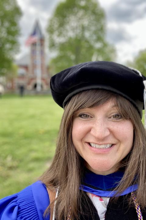 photo of Meaghan in full regalia in front of Thompson Hall at UNH