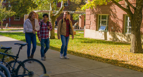 students walking on campus with bikes on bike rack in the foreground