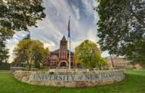 Photo of Thompson Hall clock tower at UNH with flag pole in front