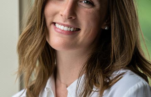 Professional headshot of Jill Durkin smiling, wearing a white button up, with a green background