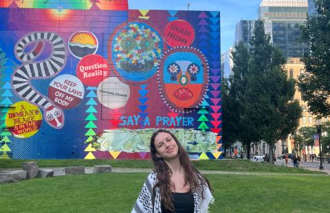 student standing outside on a lawn with a brightly colored mural in the backgroudn