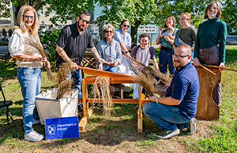 group of people outside gathered around harvested flax and tools