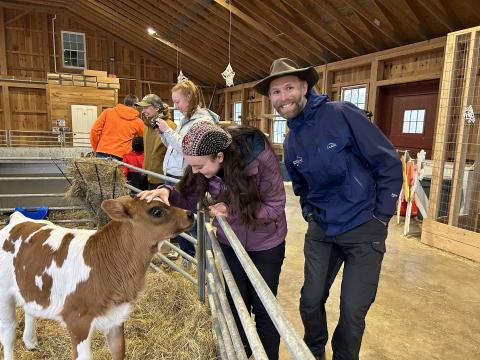man and students in a barn, one student is patting a small cow