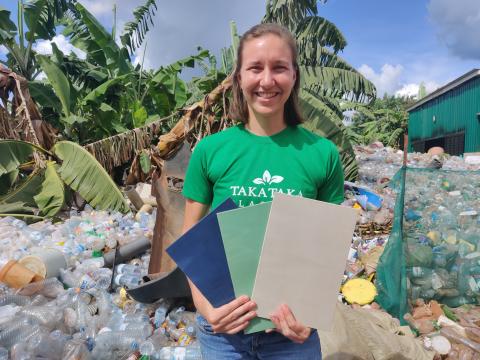 Paige outside standing in front of piles of plastic, holding a recycled plastic product