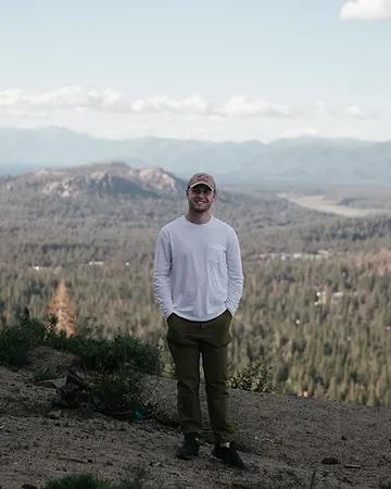 George Anderson smiling and standing on rock with a mountain in the background.