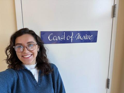 Gabi headshot standing by Coast of Maine sign