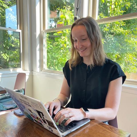 Olivia working at a laptop at a desk with windows in the background