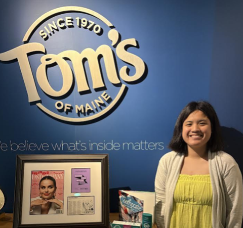 person standing near a desk with photos and a logo sign on the wall