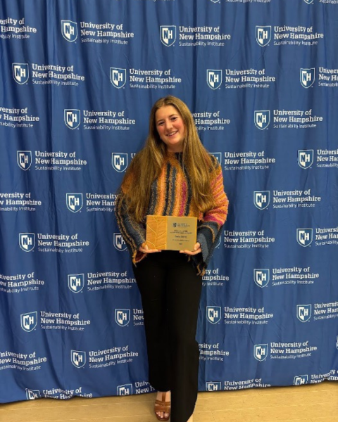 person standing holding an award with a blue step and repeat in the background