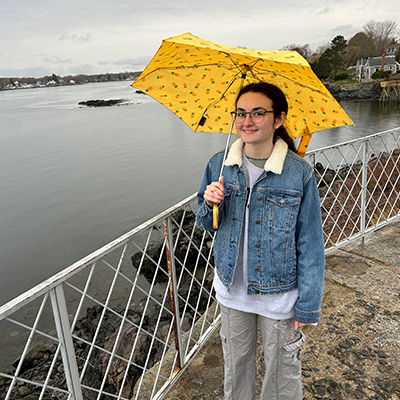 person outside on a sidewalk by the water holding an umbrella