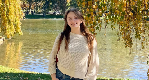 person standing outside with a body of water and trees in the background