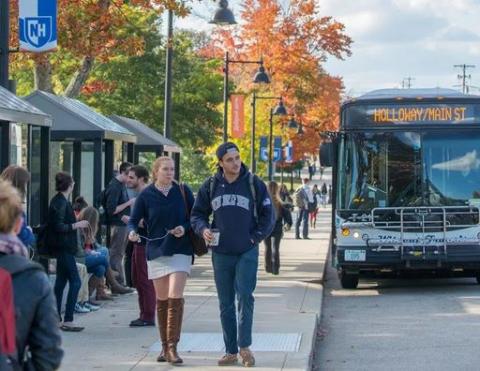 Wildcat Transit bus pulled up to Main Street Durham bus stop; students walking on sidewalk.