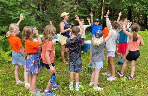 Kids in a circle at summer camp responding to a counselor.