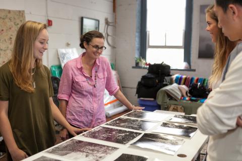 Three students and a professor looking at artwork on a table