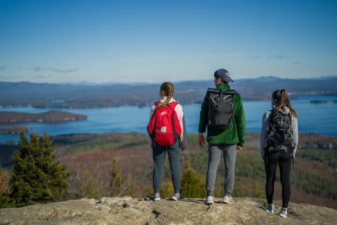 Three students standing on Mount Major looking out over the lake
