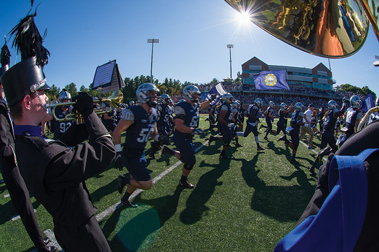 UNH marching band and football players run on the field at wildcat stadium