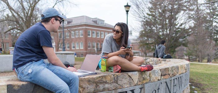 UNH students sitting on the wall in front of Thompson Hall, talking