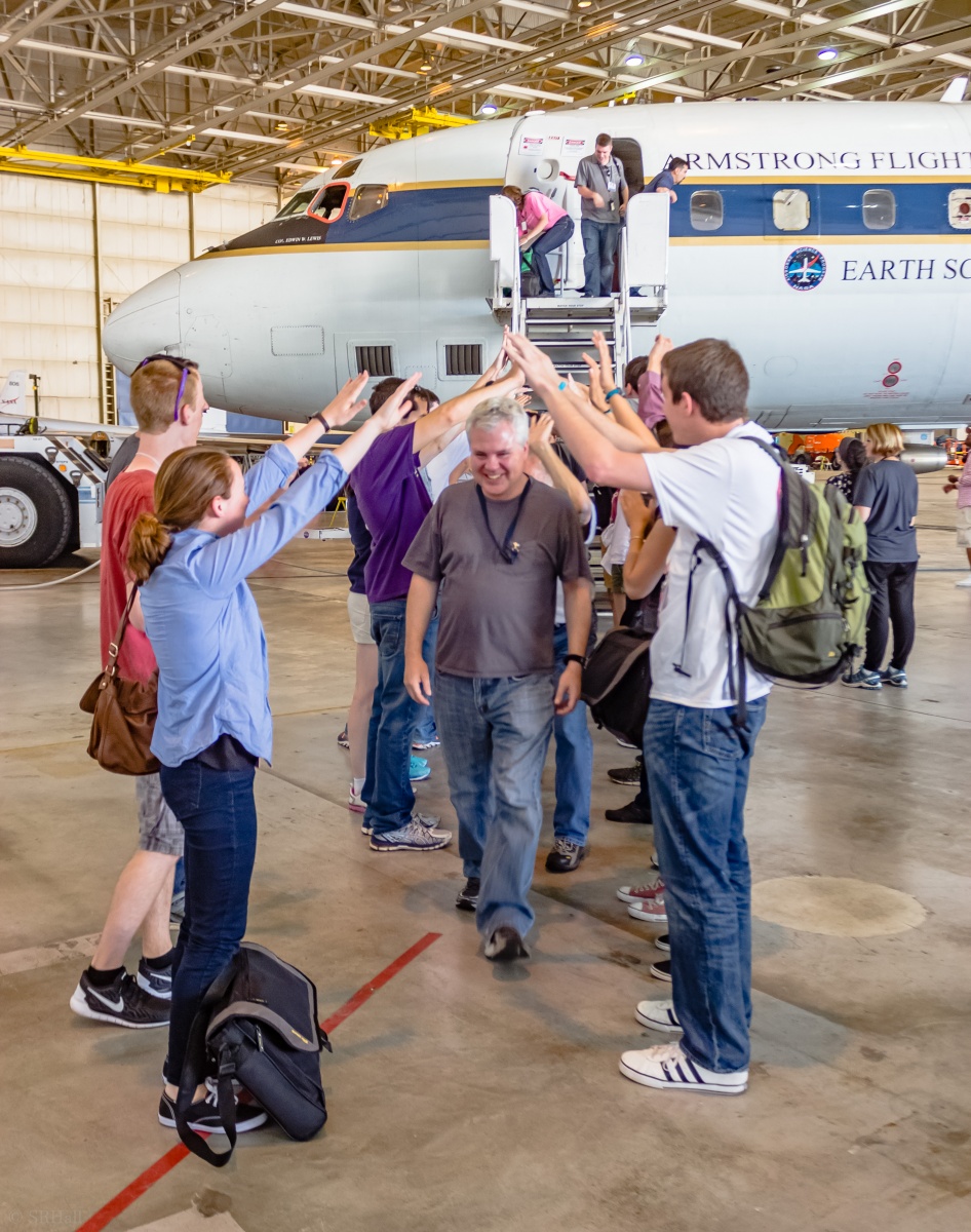 Eric Scheuer in an airplane hangar walking underneath people's arms raised in an arch.
