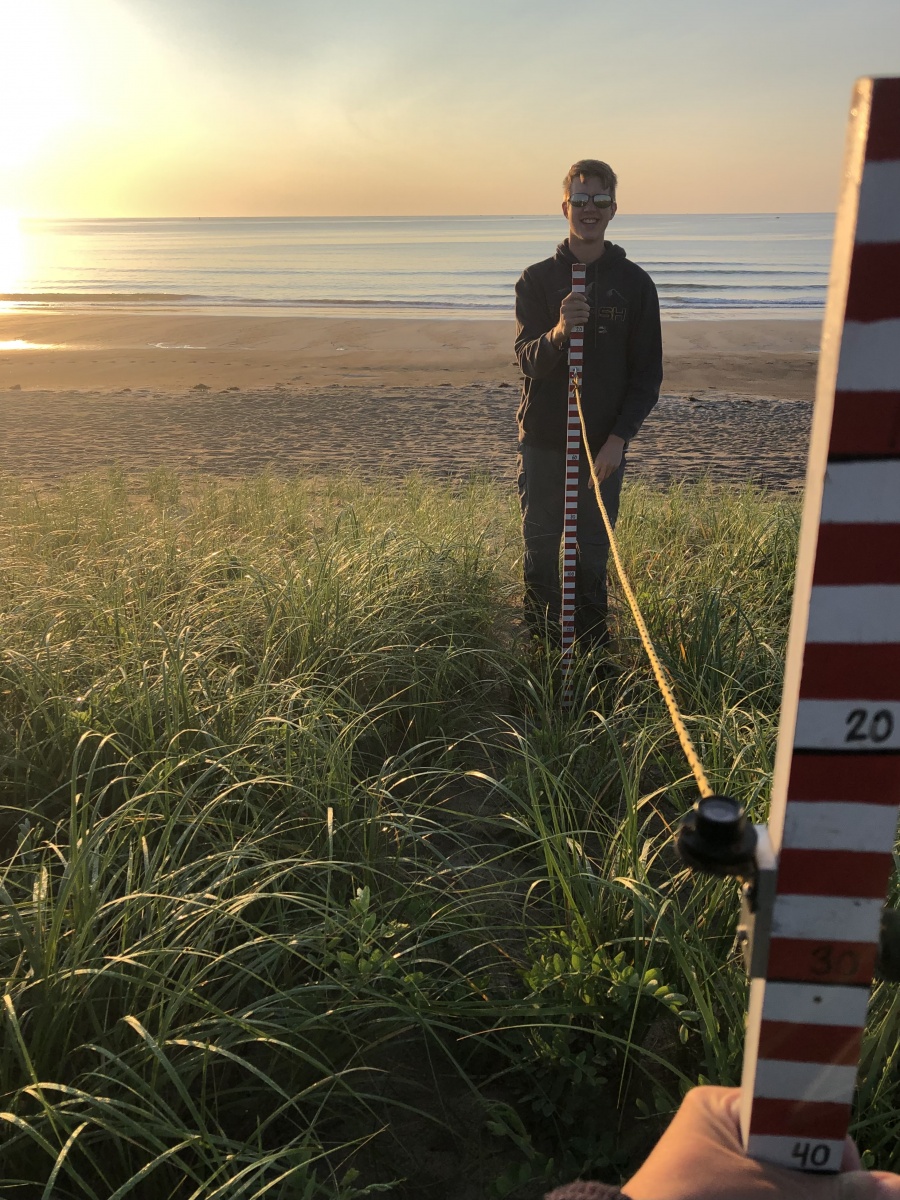 Bryce Stetson stands on a beach holding a measuring stick.