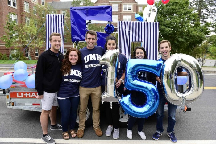 Julianne Calef '17 and other students holding UNH 150 balloons in front of a float
