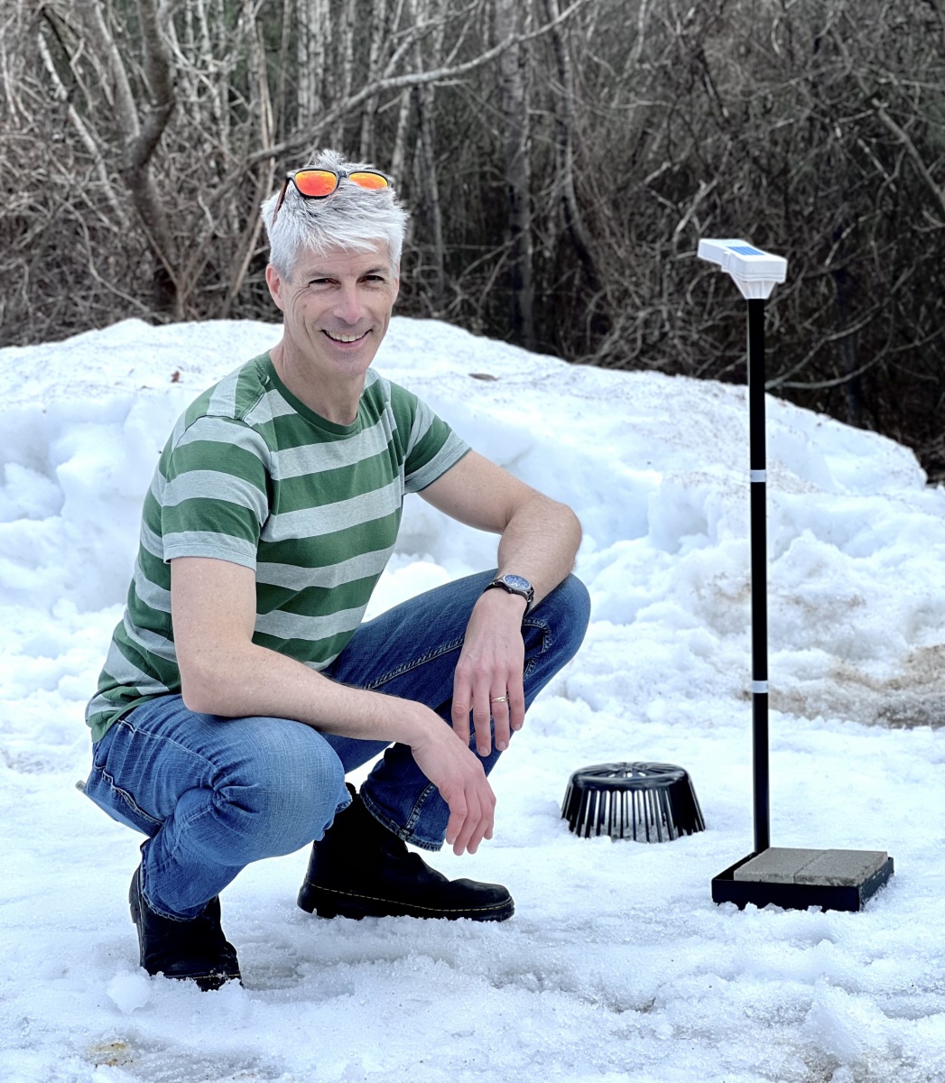Man crouches in snow next to monitoring equipment