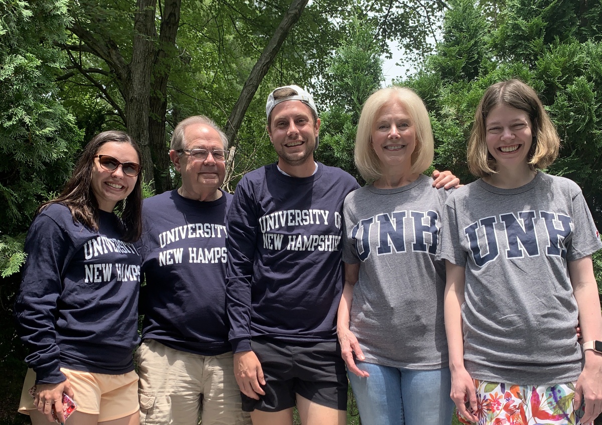 Assistant professor Adam Brockett poses with his family who are all wearing UNH shirts or sweatshirts on the UNH campus
