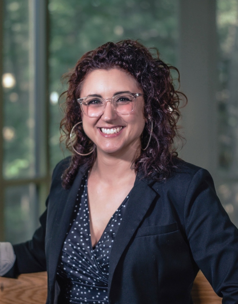 Headshot of female with curly brown hair, glasses and large hoop earrings