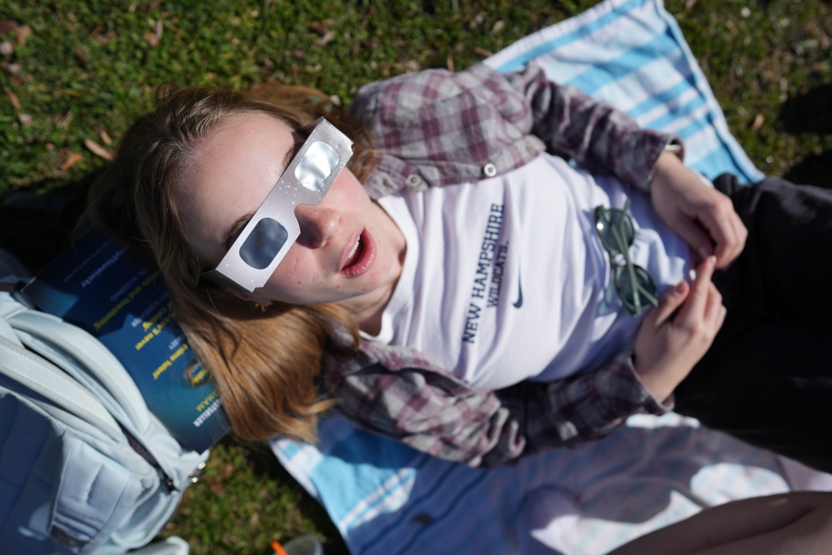 Female college student wearing eclipse glasses lies on the ground