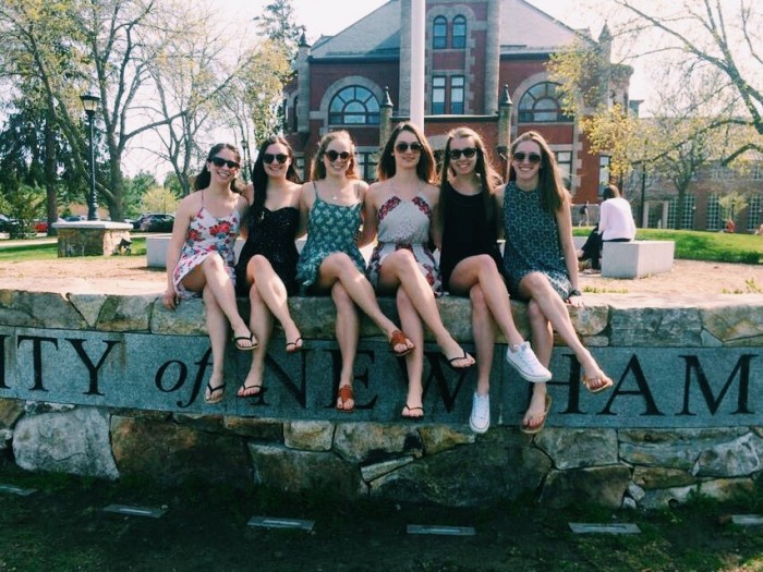 Charlotte Harris '18 and other UNH students sitting on the wall in front of Thompson Hall